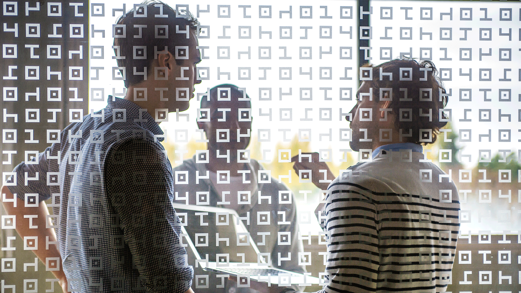 Un groupe d'hommes discute derrière une paroi en verre à motifs 