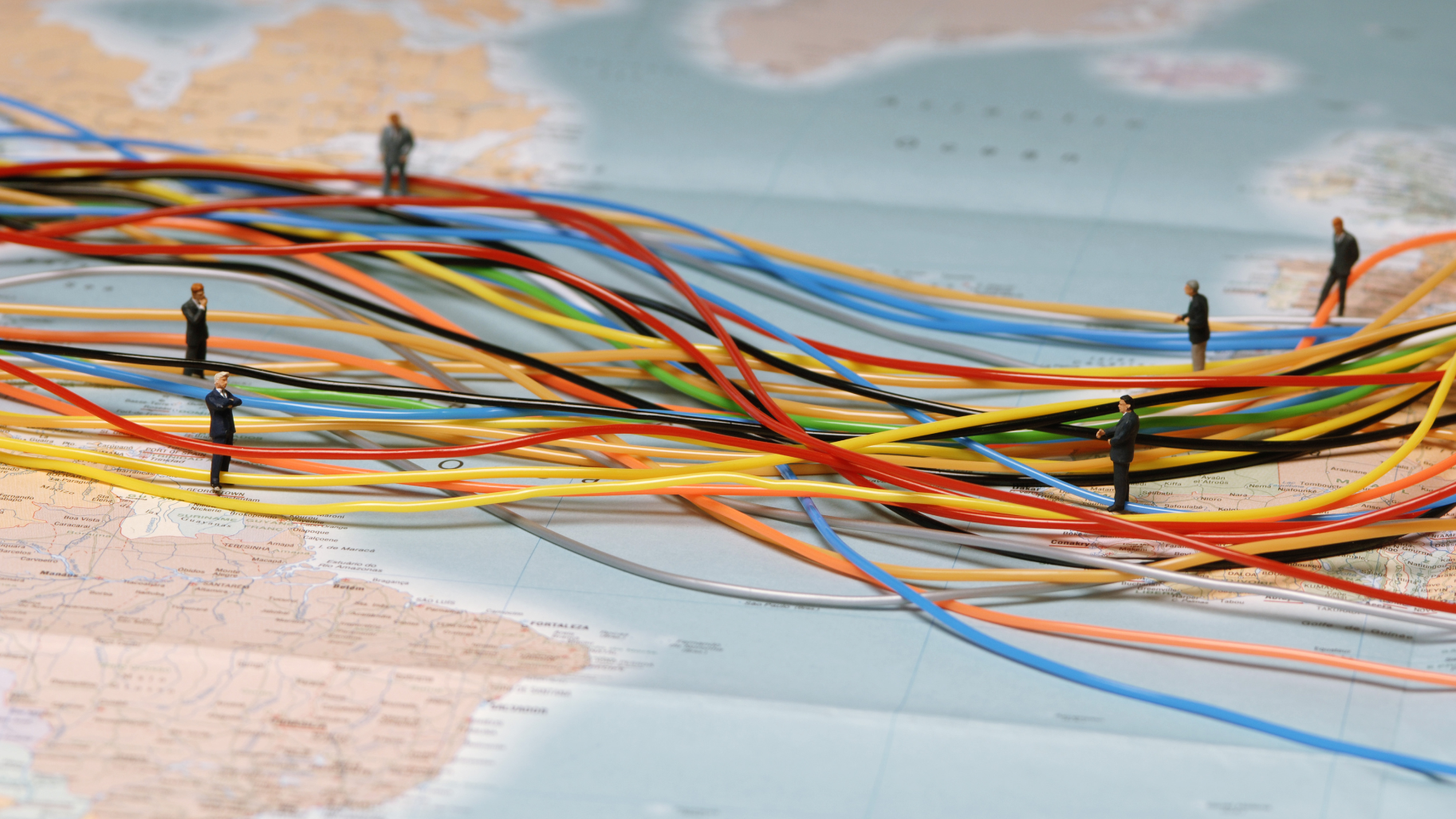 Petits bonhommes en plastque et câbles déposés sur une carte de l'Atlantique reliant les deux continents